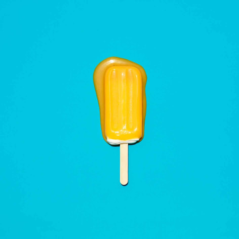 Color phtoo of an orange popsicle melting on a solid blue background.