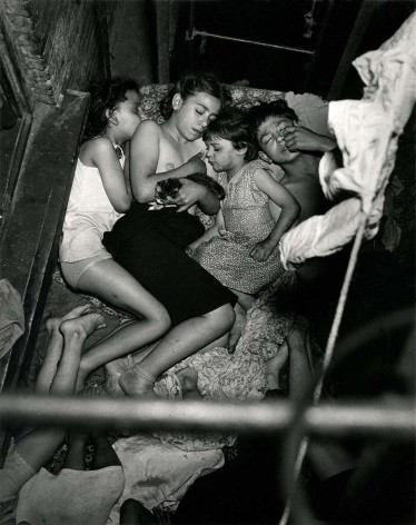 Black and white image of four children sleeping outside on a fire escape with a kitten, in a tenement on the Lower East side, summertime.