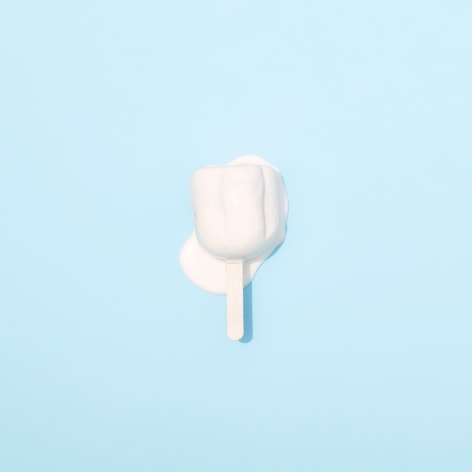 Color photo of a popsicle melting on a pale blue background.