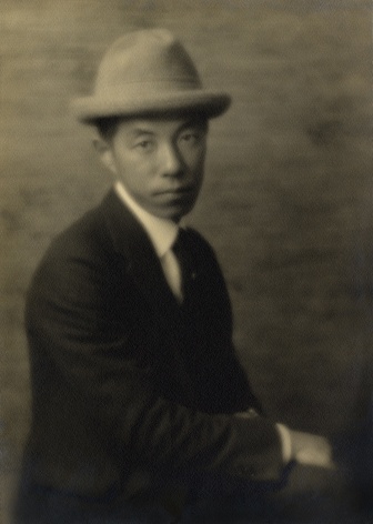 Japanse American man in a suit and light colored and narrow brimmed hat, sitting for his portrait.