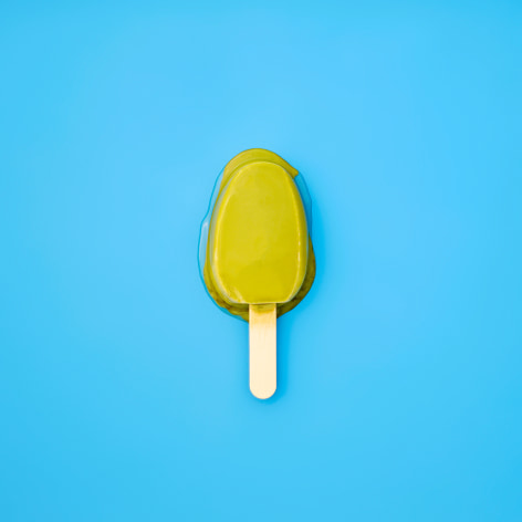 Color photo of a green popsicle melting on a blue background.
