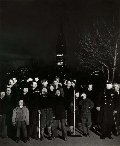 Black and white image of a crowd watching a fire, Empire State Building in the background.