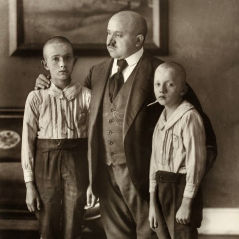 Black and white photo portrait of a father and two sons, all look sad and the boys have shaved heads like their father.