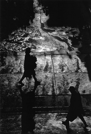 Black and white photo of silhouetted people traversing puddles of melted snow.