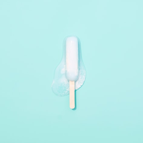 Color photo of a popsicle melting on a sea foam colored background.