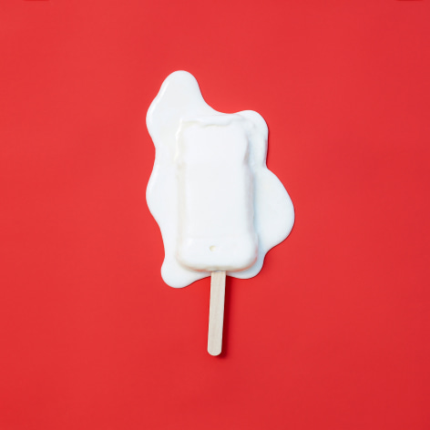 Colorful photo of a melting popsicle on a solid red background.