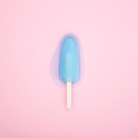 Colorful photo of a melting popsicle on a solid pink background.