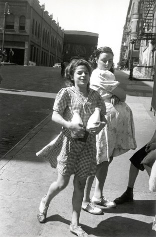 Black and white photo of a woman crossing the streets, carrying two old fashioned milk bottles and smelling, a pregnant woman behind her looks over her shoulder at her and gives her a dirty look.