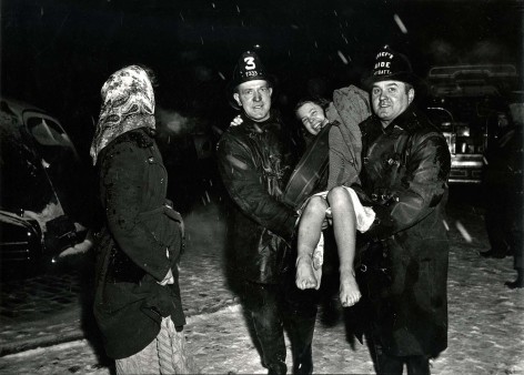 Black and white image of a smiling girl being carried through the scno wby rescung fire fighters.