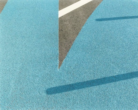 Color photo of a geometric fomr created by blue and white painted sections of asphalt