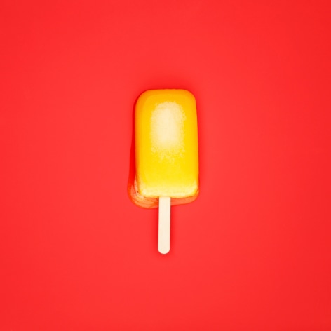Colorful photo of a melting popsicle on a solid orange background.