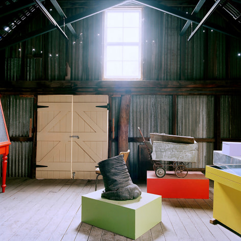 Color photo of various objects in a storage shed with light coming through a high window, a taxidermied elephant foot is in the center.