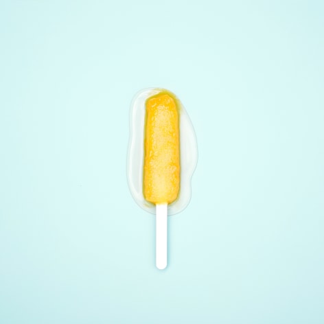 Color photo of a green popsicle melting on a blue background.