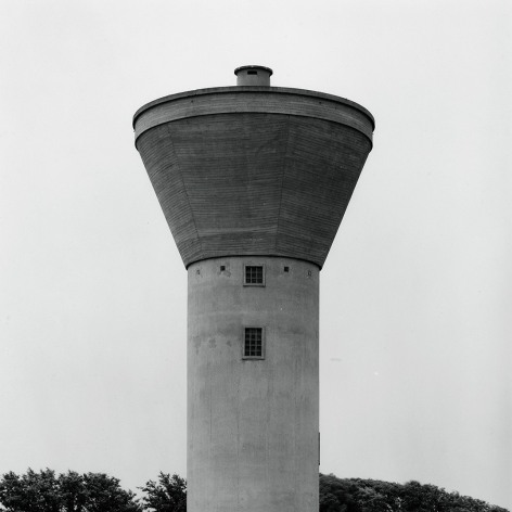 A black and white photograph of an early industrial water tower. 