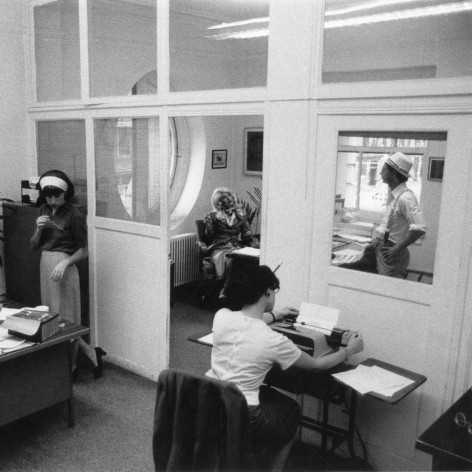 Black and white photo of office and office workers, dressed din a midcentury style.