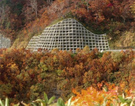 White anti-erosion structure set into a wooded hillside, the leaves on the trees are autumnal colors.