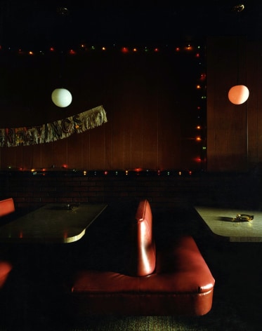 Color photograph of dimly lit old bar booths with round pendant lights and decorative tinsel on a brick wall.
