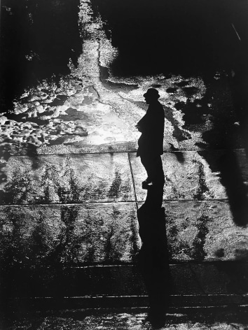 Black and white photo of a silhouetted man in a hat traversing puddles of melted snow.