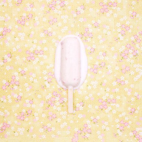 Color photo of a popsicle melting on a yellow patterned rice paper background.