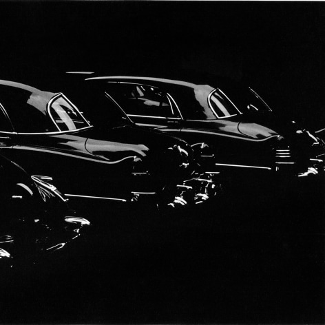 Black and white photo showing a row of 1950s cars gleaming in low light.