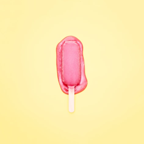 Color photo of a pink popsicle melting on a yellow background.