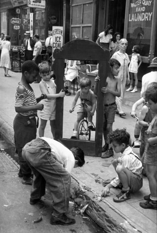 Black and white photo of a 1940s NYC street scene showing a group of young boys gathered around the large wooden frame of a broken mirror.