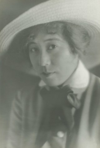 Black and white portrait of the the Japanese American film star Tsuru Aoki, she is wearing a large straw hat and a bow around her collar, she is looking at the camera