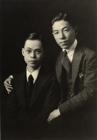 Black and white studio portrait of two well dressed Japanese American men&mdash;one man has his arm around the other.