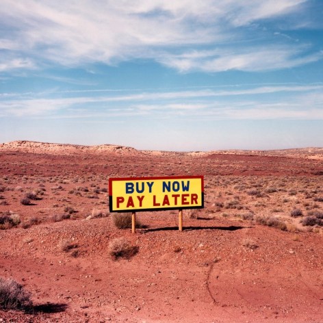 Photo of a colorful sign that reads "BUY NOW PAY LATER", standing alone in the arid Arizona desert.