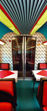 Color vertical panoramic photo of a train's dining car, interior is vibrant red and orange.