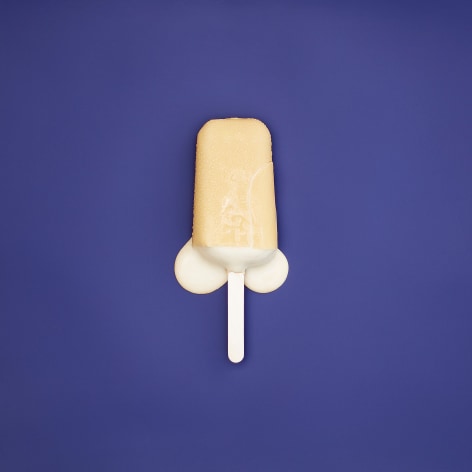Color photo of a yellow popsicle melting on a blue background.
