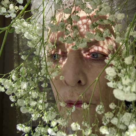 Close up self portrait of the artists—older white haired woman—looking through a Baby's Breath pant.
