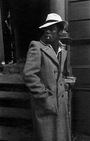 Anthony Barboza, man wearing a trench coat and hat, smoking a cigarette, in Harlem 1970.