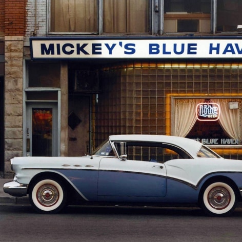 Color image a blue classic 1950s car in front of a working g class bar with a sign that reads Mickey's Blue Haven.