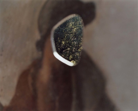 Color photo of a reproduction of a painting with the face cut out, a tree is seen through the hole.