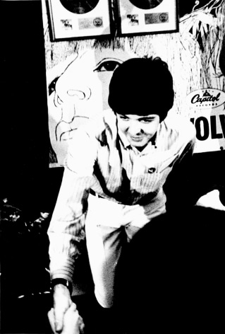 Black and white image from a Beatles press conference in 1966. Paul Mccartney reaches out to shake a hand.