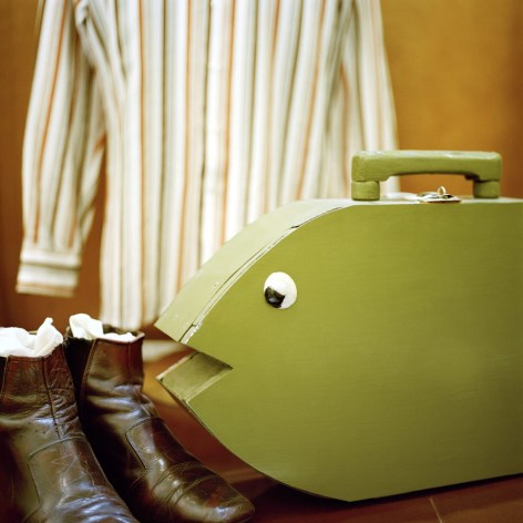 Color photo of cowboy boots and a striped shirt with a green wooden guitar case that is made to resemble a fish.