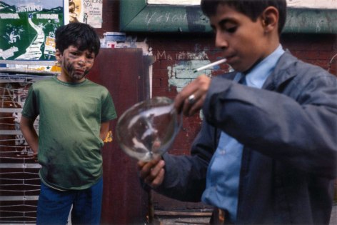 Color photograph of two boys, one with a dirty face watches the other play oath a bubblle
