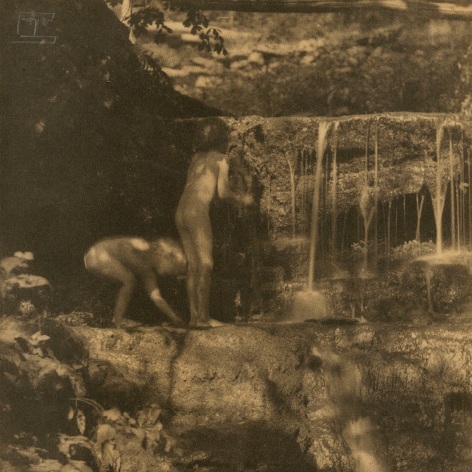 Warm toned black and white photo of two nude children playing on a rocky waterfall.