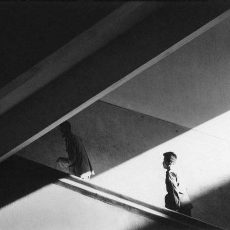 Black and white photograph of two men in Hong Kong ascending a mid-century modernist stairwell in slanting light.