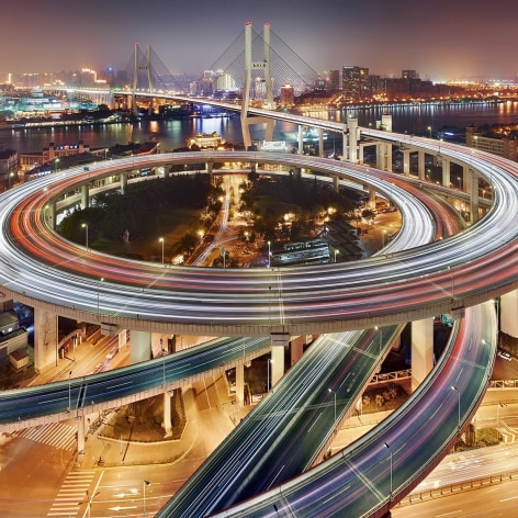 Long exposure photograph of cars driving on the spiral ramp of a Shanghai bridge.