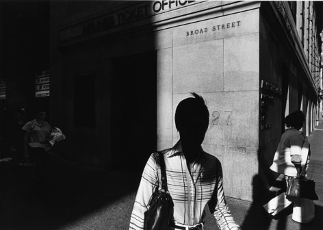 Starkly lit black and white photo showing the silhouette of a woman on a city sidewalk.