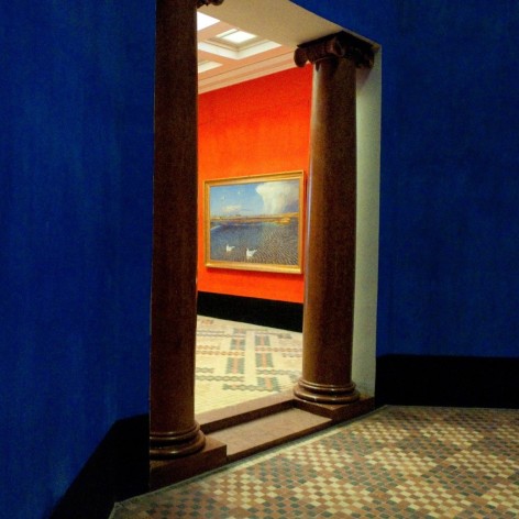 Color photo of a view from one room to another in a museum, looking from a blue room to a red room at a painting, over tiled floor.