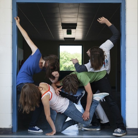 Color photo of four high school students crowded into a a school doorway and contorting their bodies together.