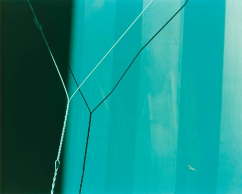 Color photo of a section of intertwined wire casting a shadow on a blue wall.