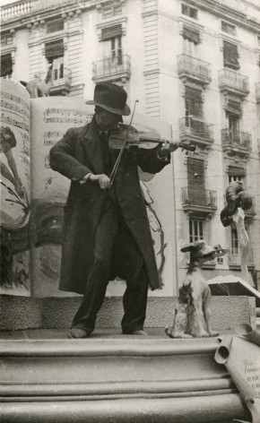 Black and white photo of an old man playing a violin in a public square in Valencia, Spain&mdash;early 20th century