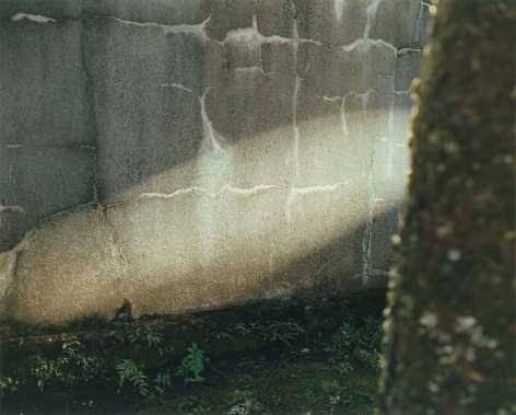 Color photo of a beam of light falling on an exterior cement wall.