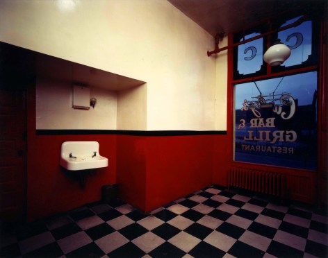 Color photograph of an emptied out former restaurant with a red and white checkered floor and sign on the window that reads &quot;Curley's Bar and Grill&quot; .