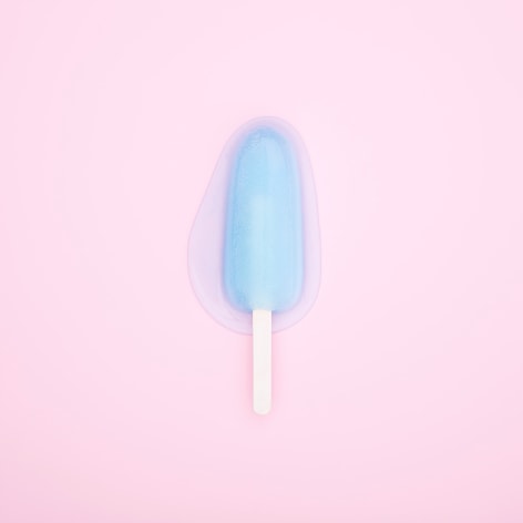 Color photo of a blue popsicle melting on a pink background.