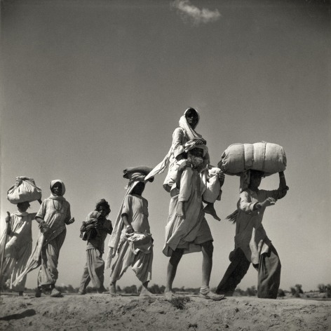 Low angled black and white photo of refugees walking across a desert landscape.